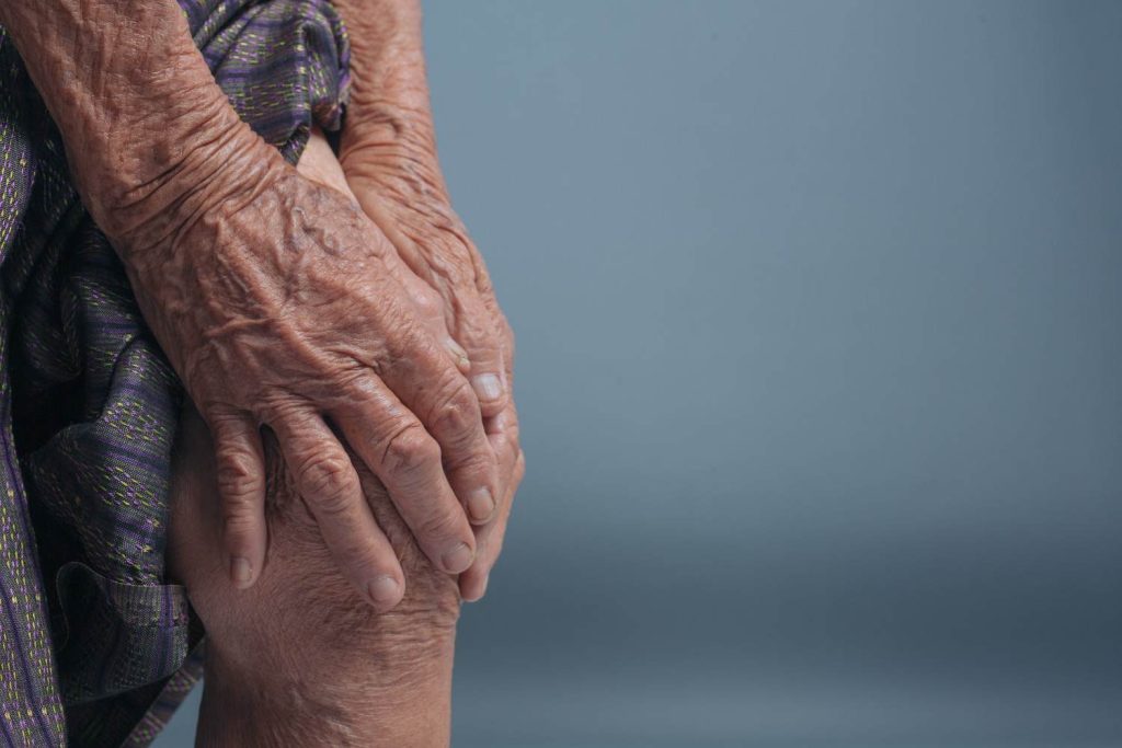 Elderly woman holding painful knee showing possible gout-related joint pain